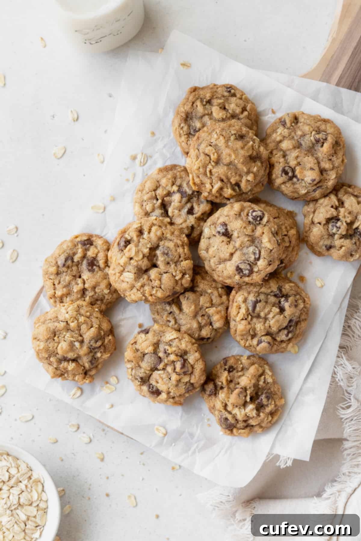 Gluten free oatmeal cookies on a parchment paper with oats scattered around.
