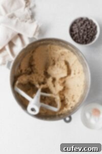 Wet ingredients for gluten free cookies in a metallic bowl with a bowl of chocolate chips beside it.
