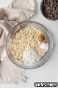 Dry ingredients for oatmeal cookies in a glass bowl next to a natural linen.