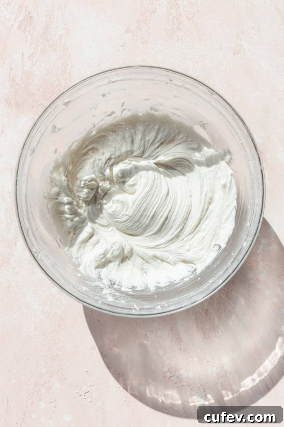 Autumn Spiced Pumpkin Squares 11 Smooth and creamy cream cheese frosting in a glass bowl, ready to be spread, resting on a soft pink surface.