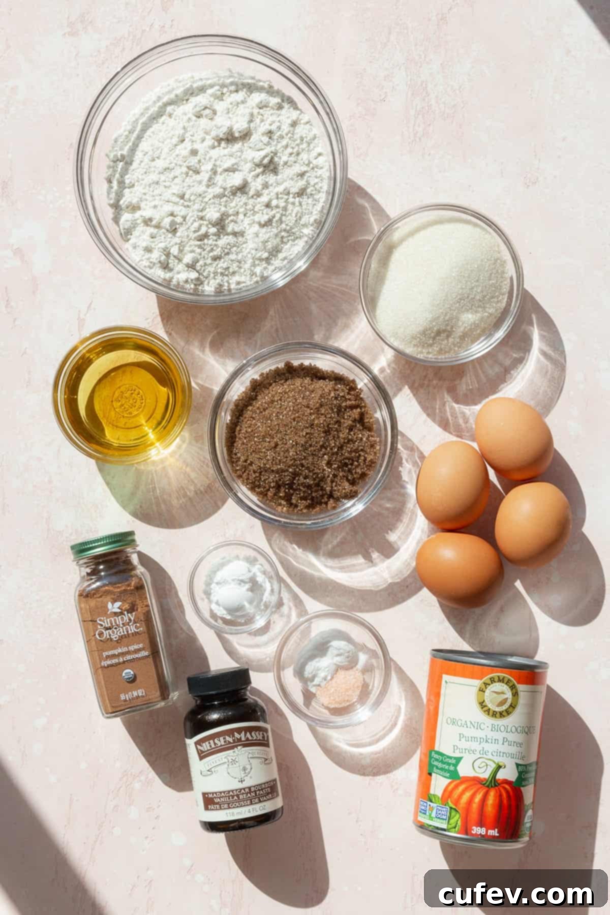 Autumn Spiced Pumpkin Squares 3 A colorful array of dry ingredients for pumpkin bars, including flour, spices, and sugar, laid out on a pink surface.