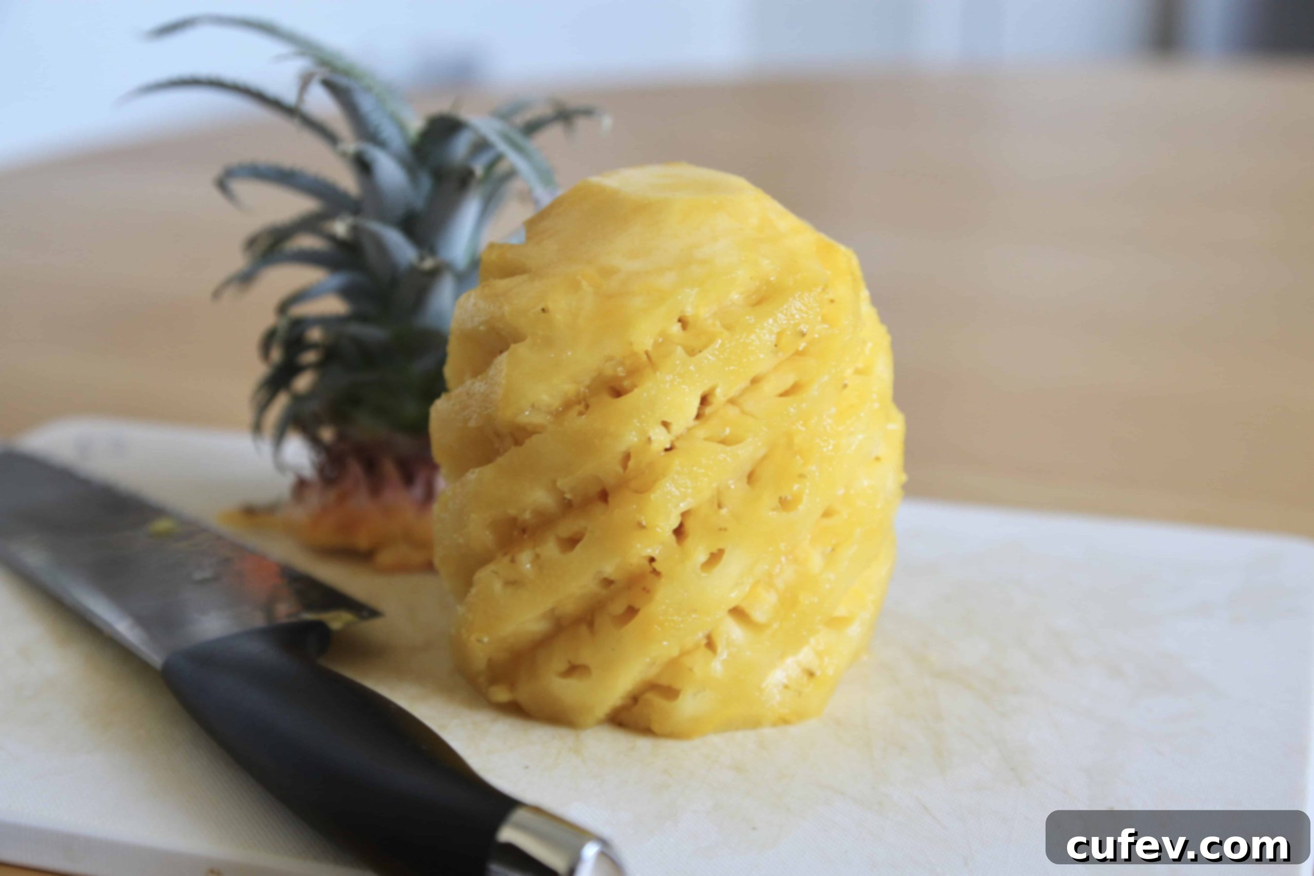 A peeled fresh pineapple on a cutting board with a knife beside it, ready for chopping.