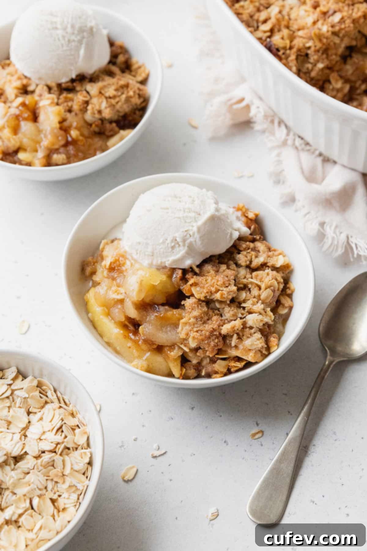 Comforting Gluten-Free Apple Crumble 2 Gluten-free apple crisp with vanilla ice cream in a small white bowl next to a spoon with more bowls placed nearby.