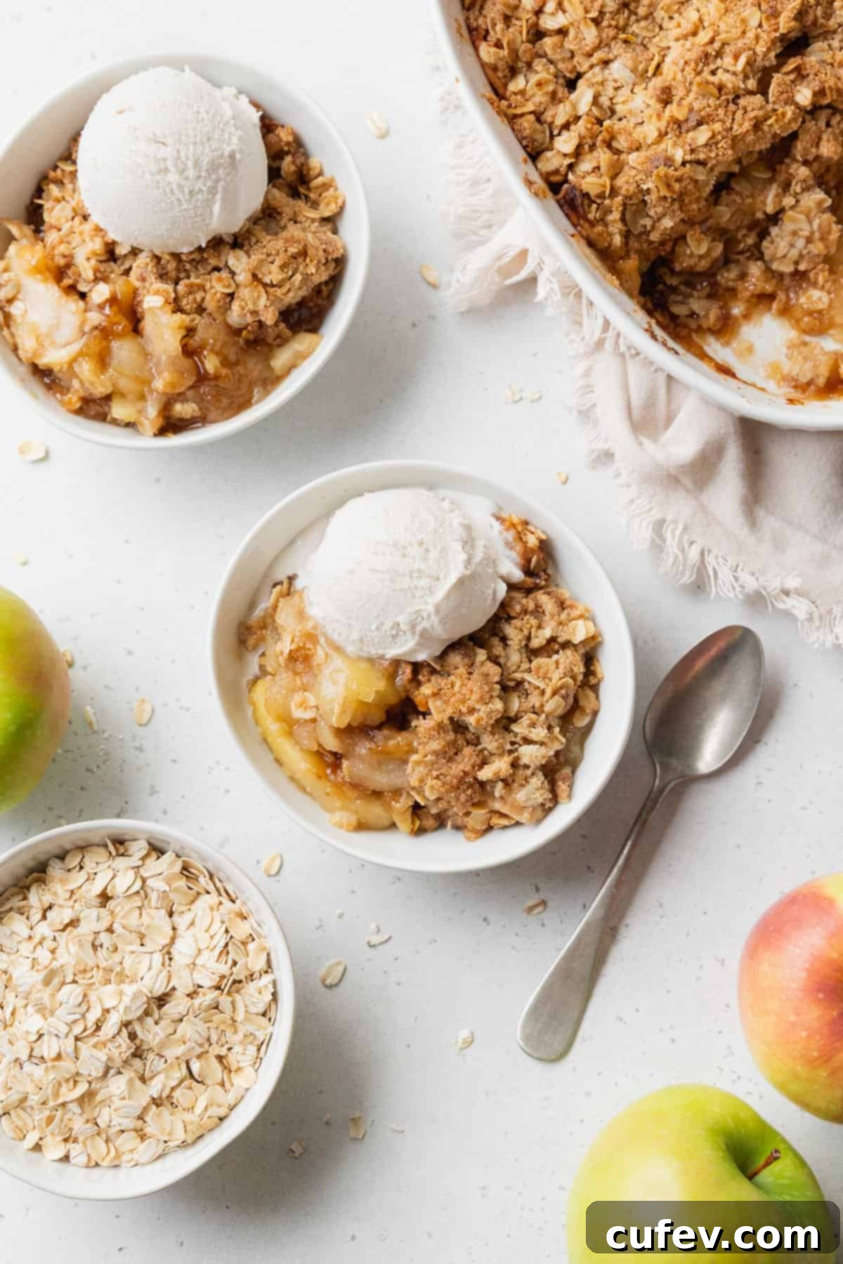 Comforting Gluten-Free Apple Crumble 4 Two bowls of gluten free apple crisp with vanilla ice cream, and a baking dish of more apple crisp placed nearby.