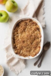 Comforting Gluten-Free Apple Crumble 9 Baked apple crisp on a beige linen with a spoon, fork, and some green apples placed next to it.
