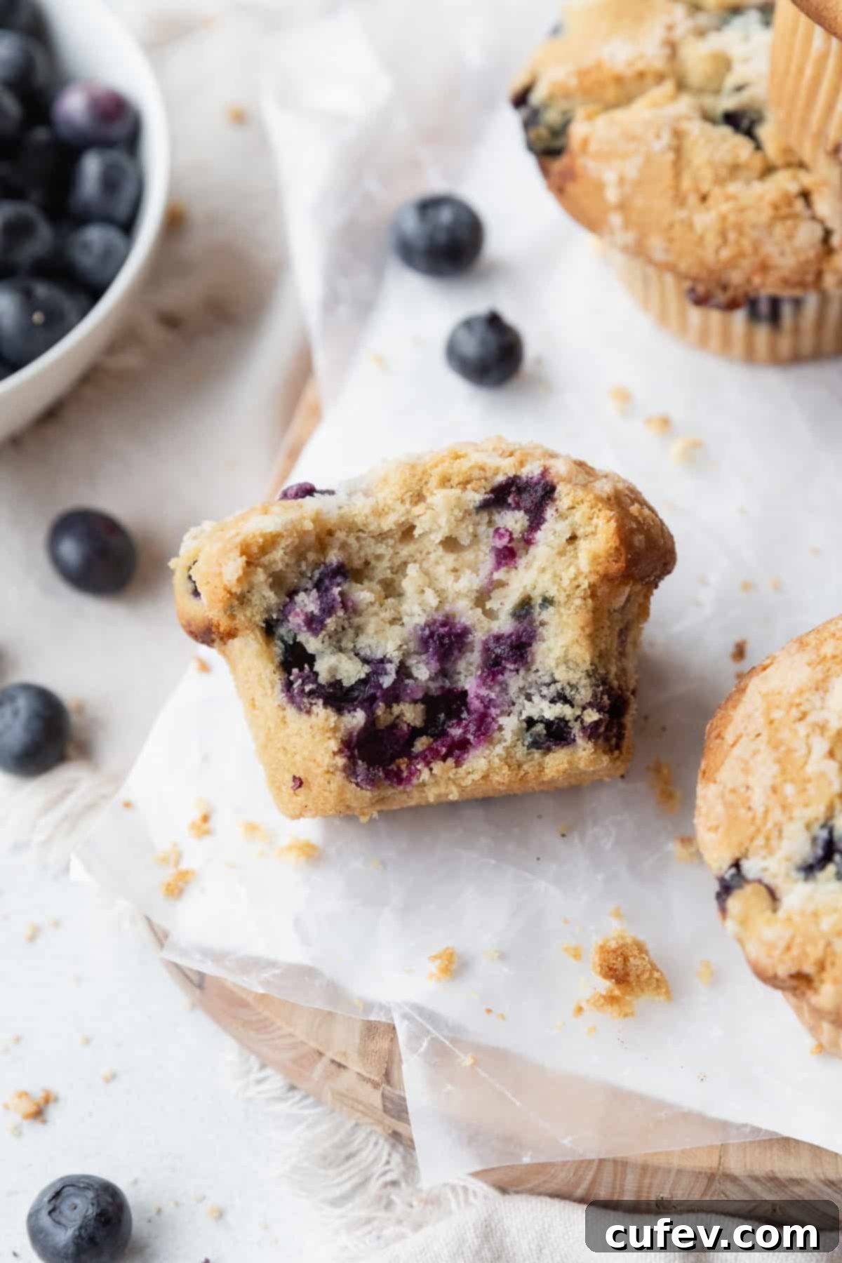A bitten blueberry muffin on its side, showing specks of juicy blueberries inside.