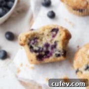 A bitten gluten free blueberry muffin laying on its side on parchment paper.