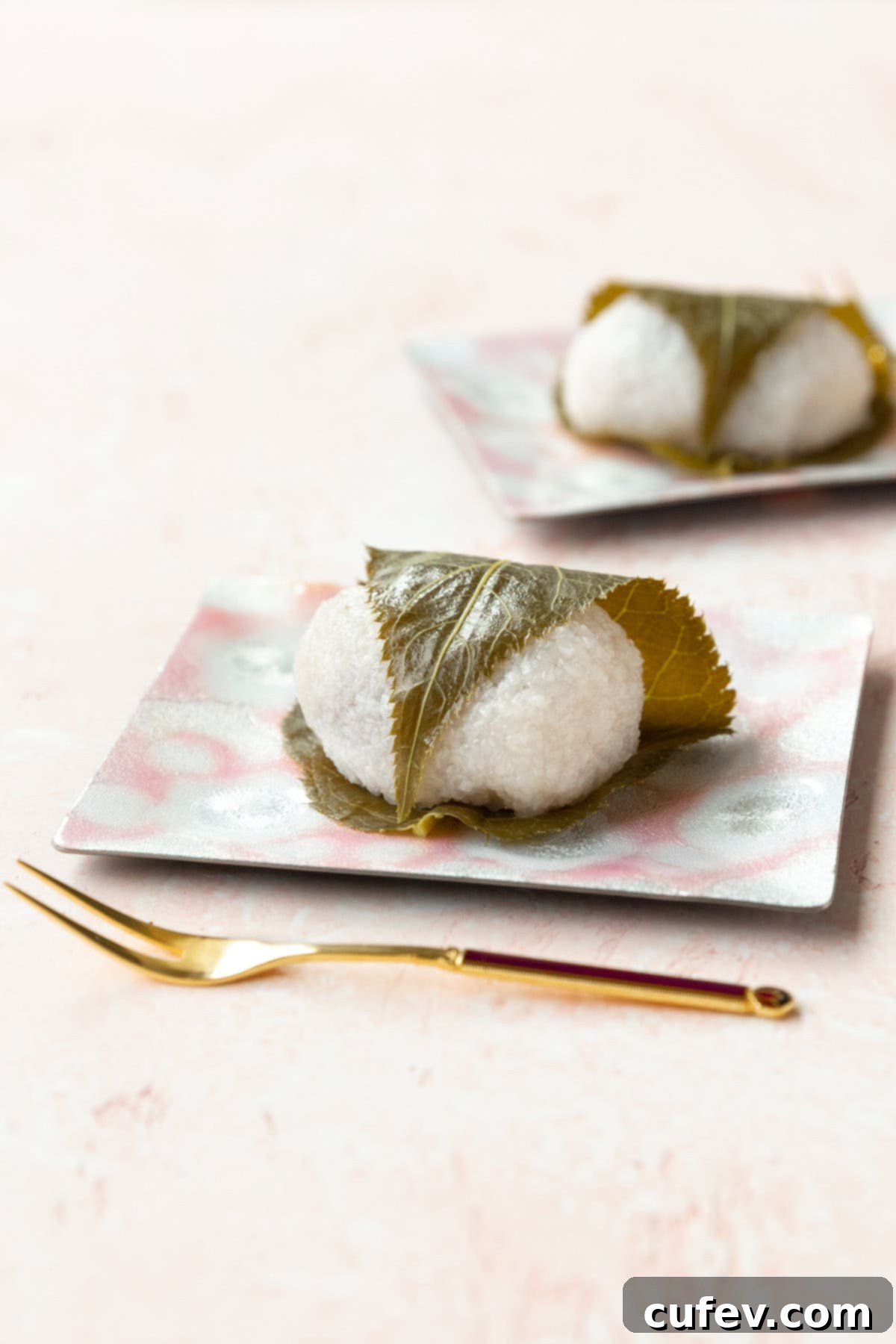 Sakura mochi on a pink dessert plate on a pink surface.