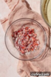 Diced fresh strawberries, lightly coated in a dusting of flour, are presented in a clear glass bowl, ready to be incorporated into the waffle batter for even distribution and enhanced texture.