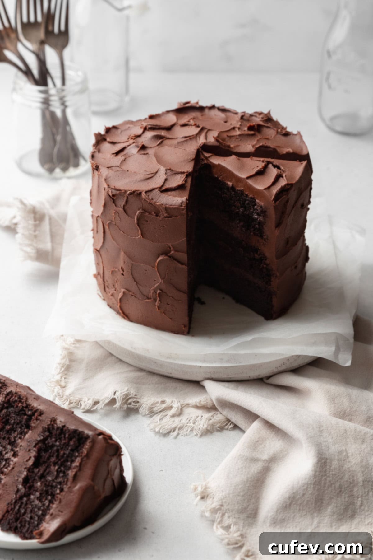 A beautifully frosted chocolate cake with one perfect slice already removed, showcasing its moist layers. Another slice is artfully placed on a small plate in front, ready to be enjoyed.