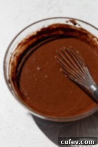 Smooth gluten-free chocolate cake batter in a mixing bowl with a whisk, after incorporating all ingredients and hot coffee.