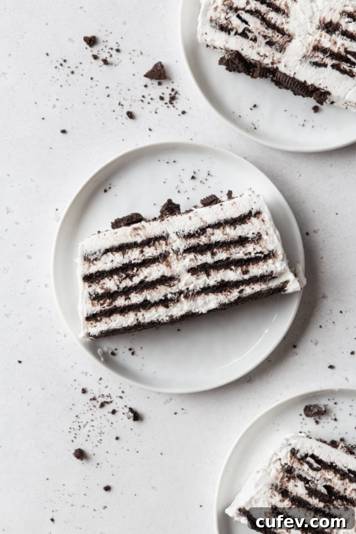 Velvet Chill Cake 2 Three perfectly sliced pieces of icebox cake, layered with chocolate cookies and cream, served on white dessert plates arranged on a soft light grey surface.