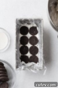 Velvet Chill Cake 5 Chocolate cookies being arranged in a loaf pan, carefully placed over a layer of creamy white filling to begin building an icebox cake.