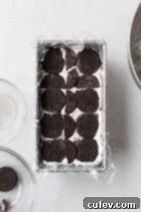 Velvet Chill Cake 7 More chocolate cookies being carefully placed over a layer of cream, some broken to fit, ensuring a complete and even cookie layer for the icebox cake.