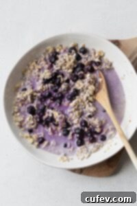 Wholesome Blueberry Overnight Oats 5 Blueberry overnight oats being mixed together in a white bowl with a wooden spoon, showing the stirring process.