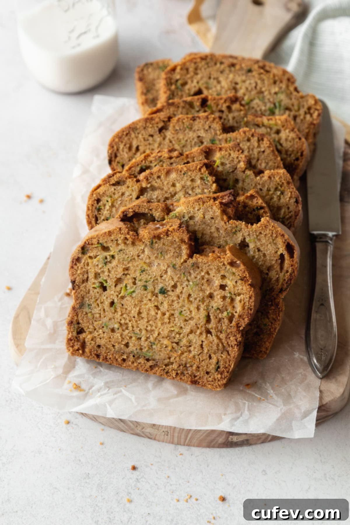 Slices of gluten free zucchini bread on a parchment lined wooden board, with a silver knife beside it.