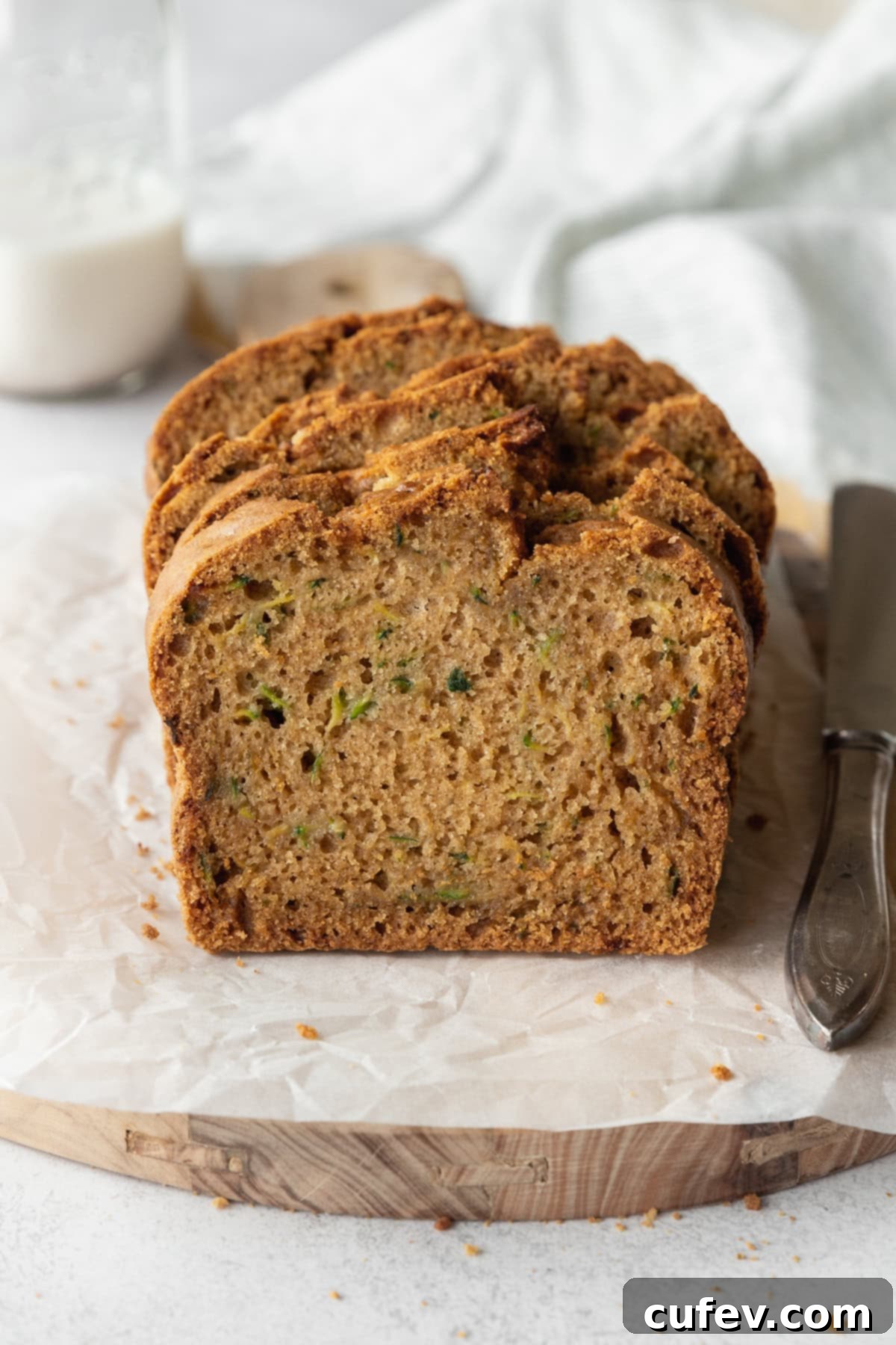 A sliced zucchini loaf on a piece of parchment paper, with a bottle of milk in the background.