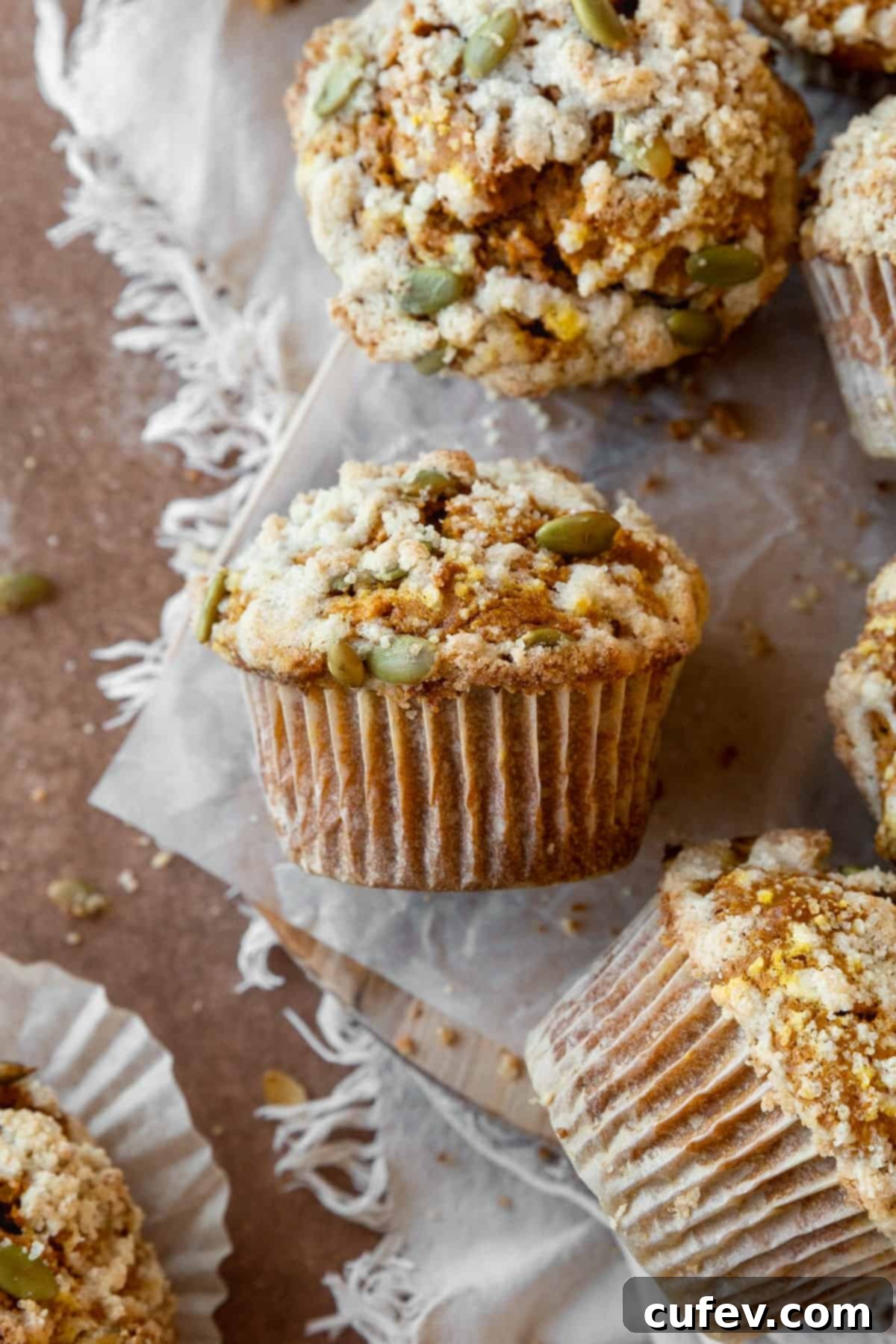 A gluten-free pumpkin streusel muffin on its side with more muffins around it, showcasing its fluffy texture and crunchy topping.