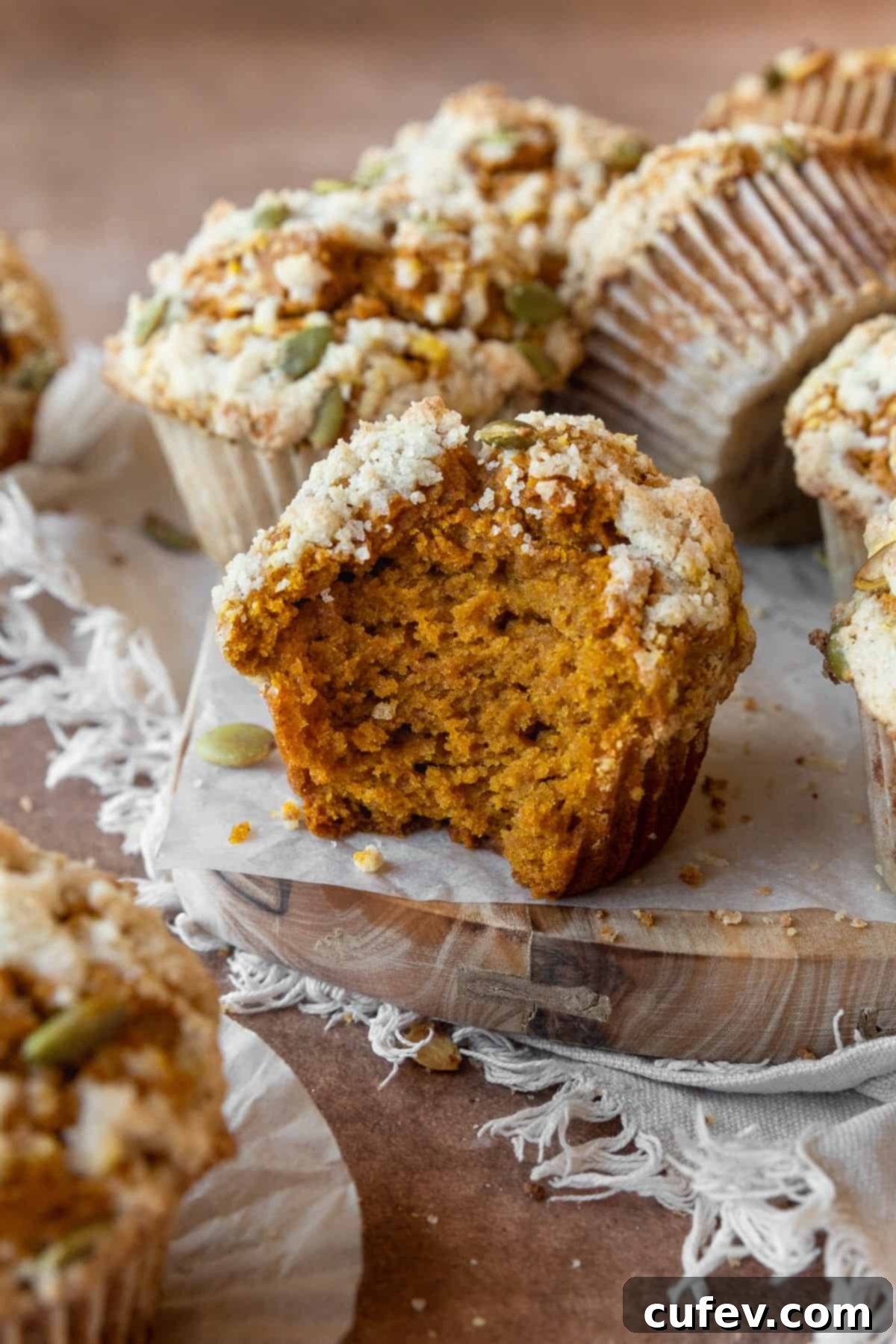 A gluten-free pumpkin muffin with a bite taken out, showcasing its moist interior, with more streusel-topped muffins around it.