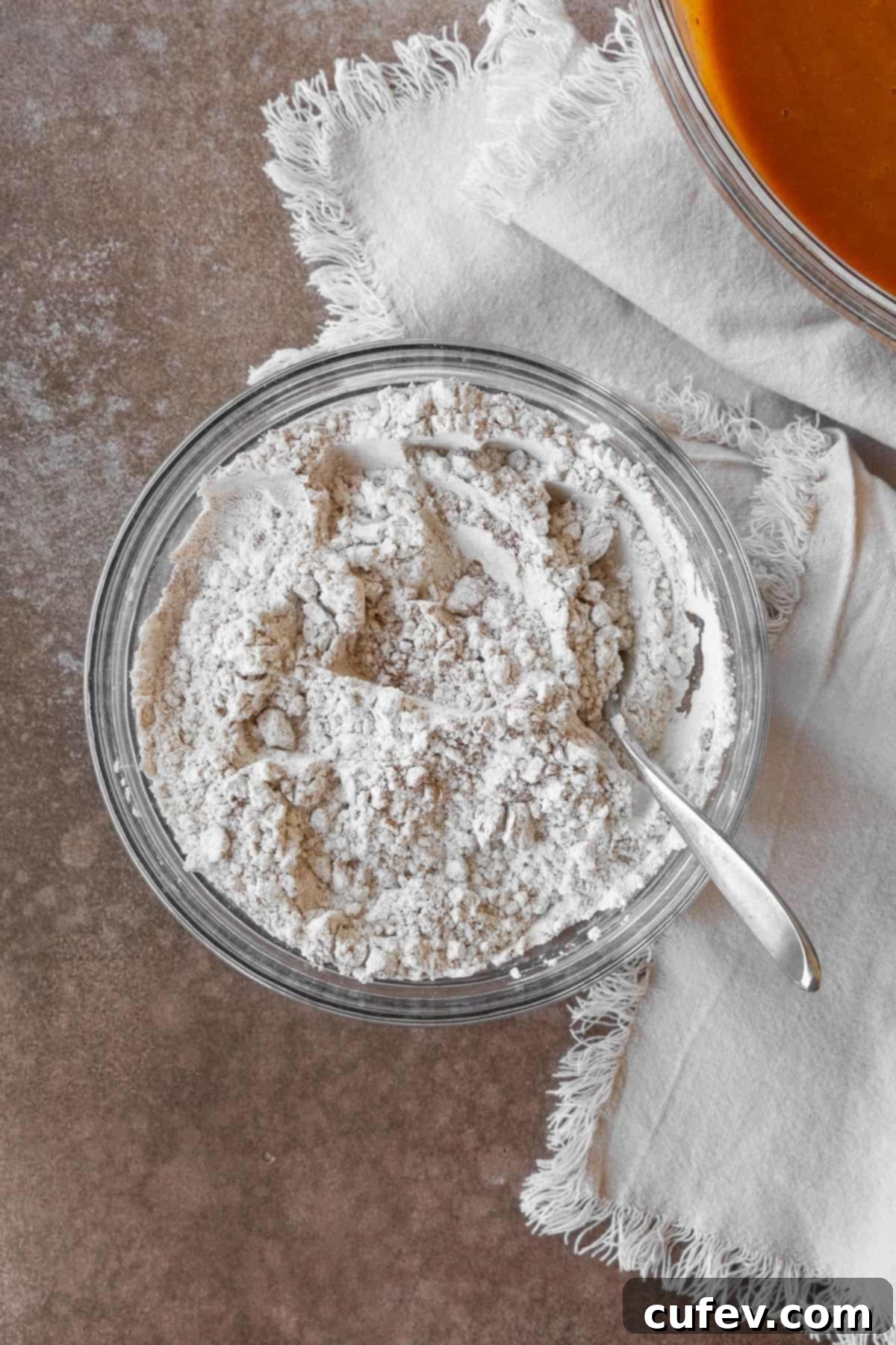 A glass bowl containing dry ingredients for pumpkin muffins, including flour and spices.