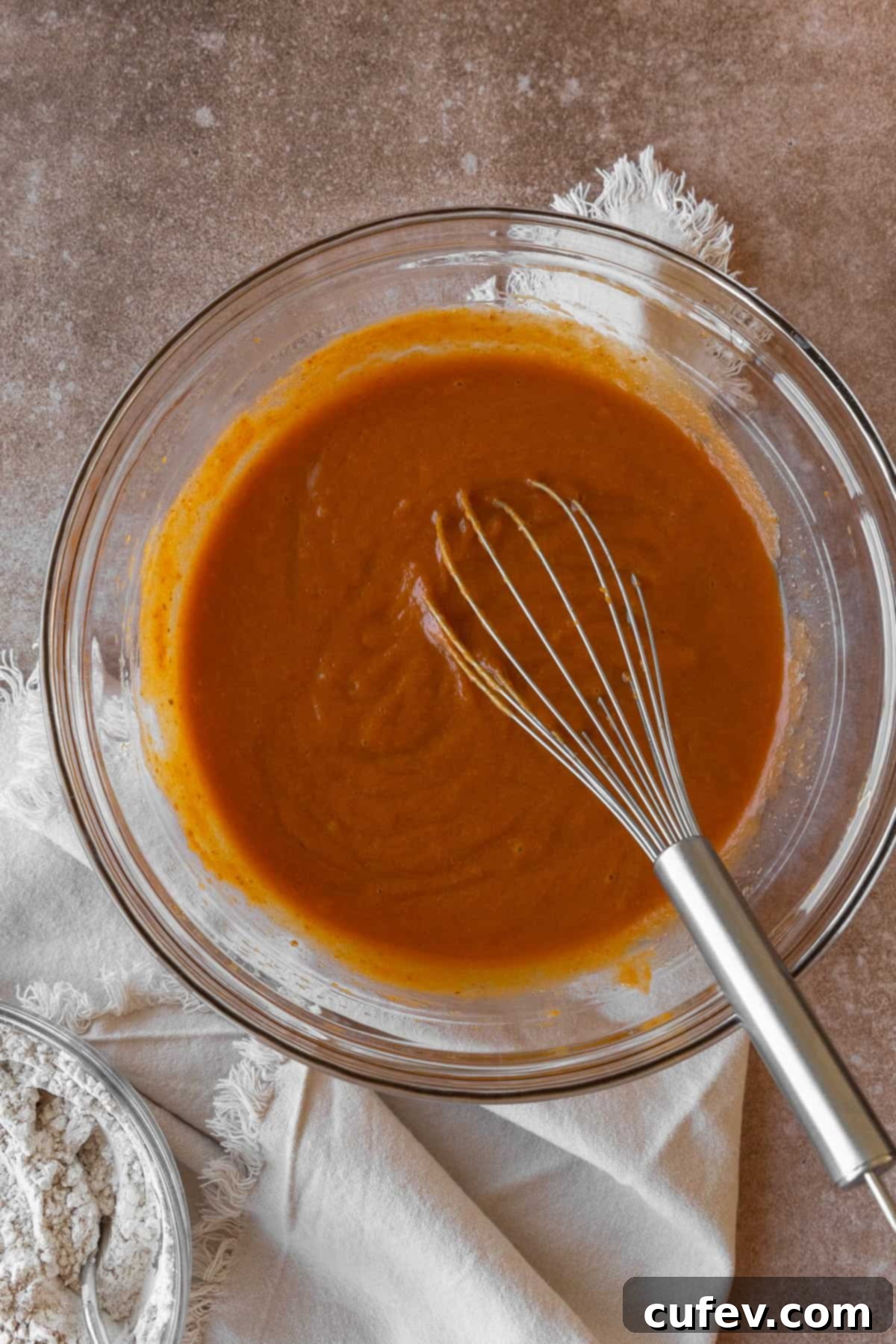 Wet ingredients for pumpkin muffins in a glass bowl with a wire whisk, creating a smooth mixture.