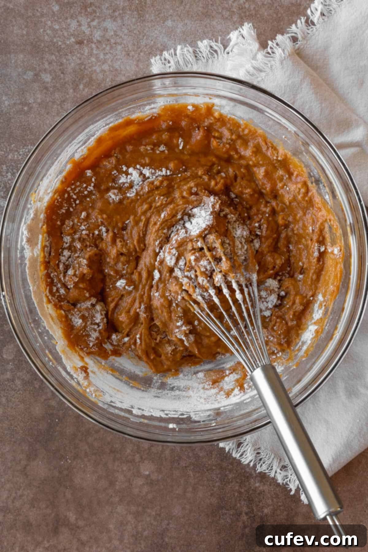 A close-up of gluten-free pumpkin muffin batter being whisked together in a glass bowl until smooth.