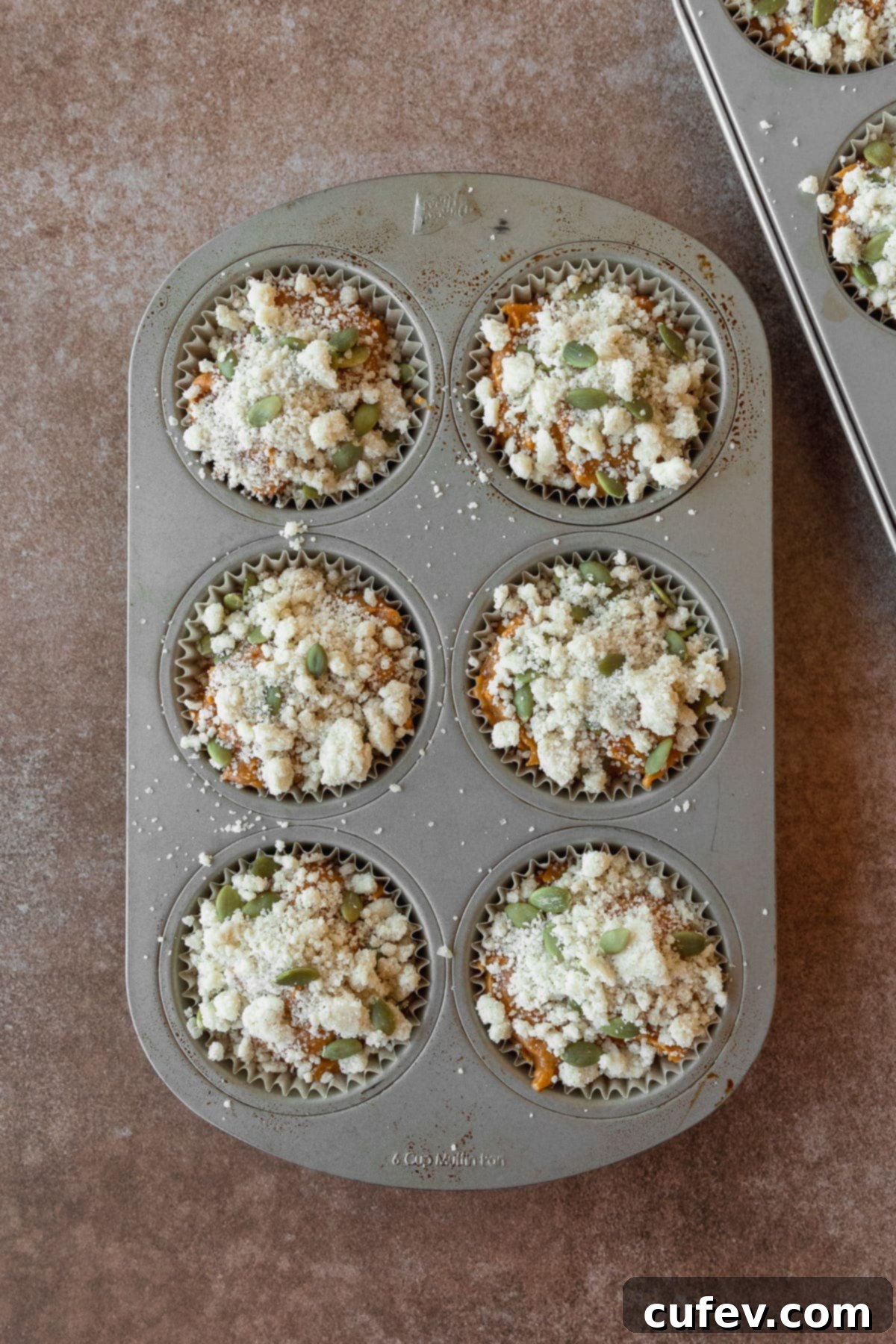 Pumpkin muffin batter topped with streusel in a muffin pan, ready for baking.
