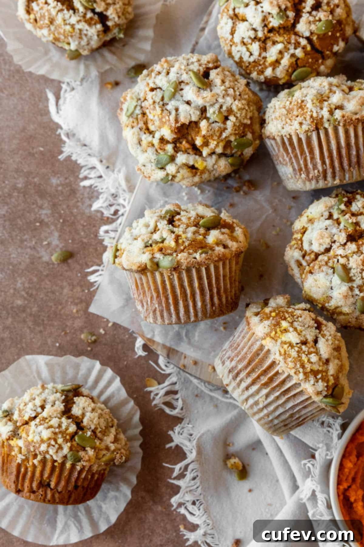 A cluster of gluten-free pumpkin muffins with streusel topping scattered on a piece of parchment paper, with some muffins placed sideways.