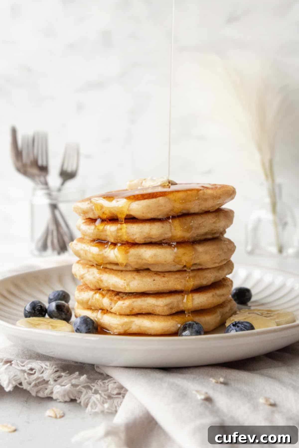 A stack of golden brown oatmeal pancakes adorned with fresh blueberries and glistening maple syrup being drizzled generously over them.