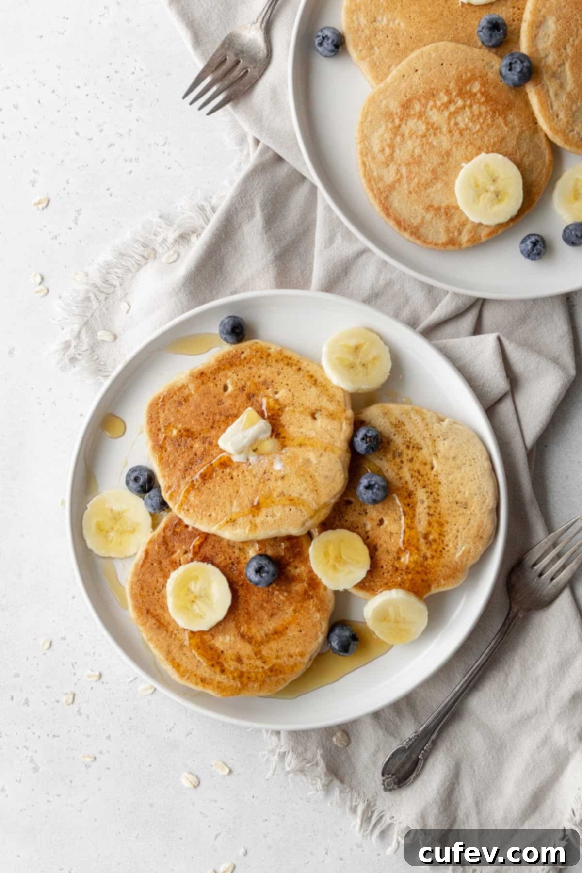 Two inviting plates of oatmeal pancakes, one topped with vibrant banana slices and the other with fresh blueberries, ready to be enjoyed.