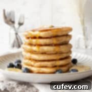 A stack of oatmeal pancakes on a plate with maple syrup being poured on top.