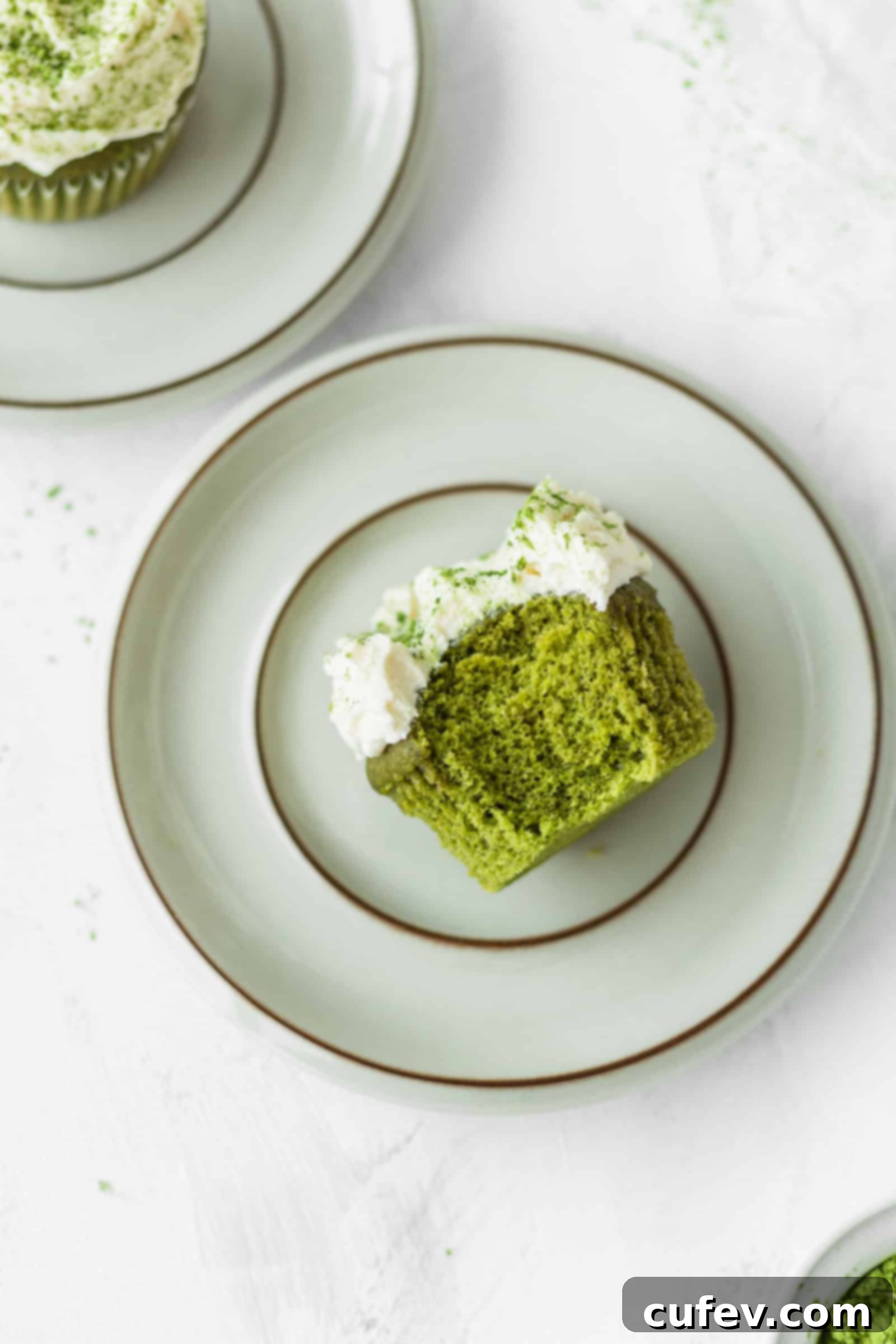 Half-eaten fluffy matcha cupcake with white chocolate frosting on a plate, showing green interior