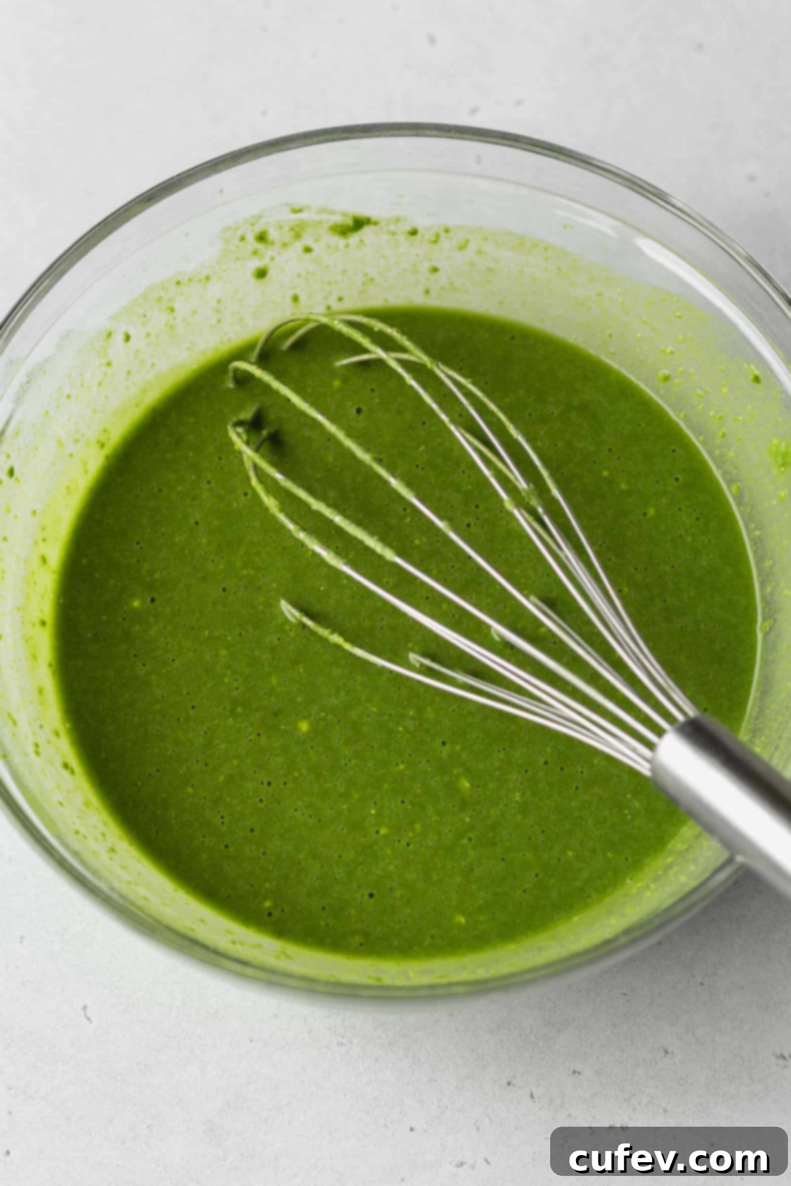 Bowl of vibrant green matcha cake batter with a whisk