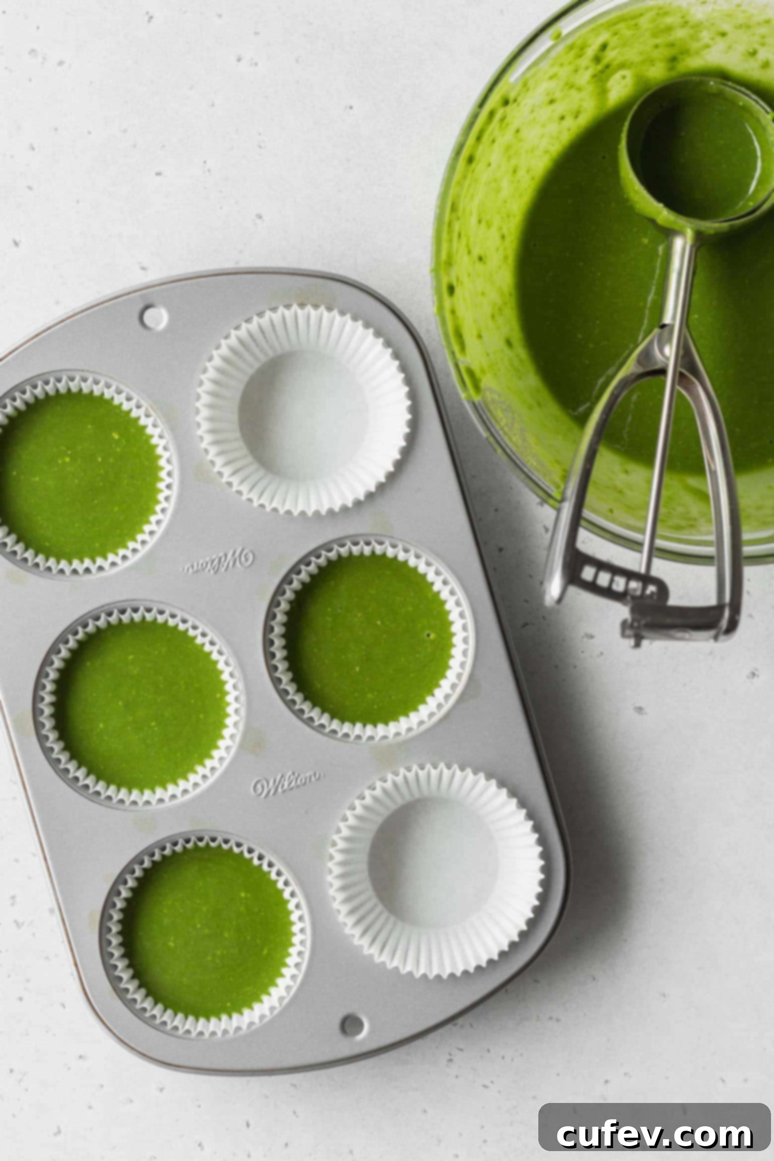 Pouring matcha cake batter into muffin pan with an ice cream scoop
