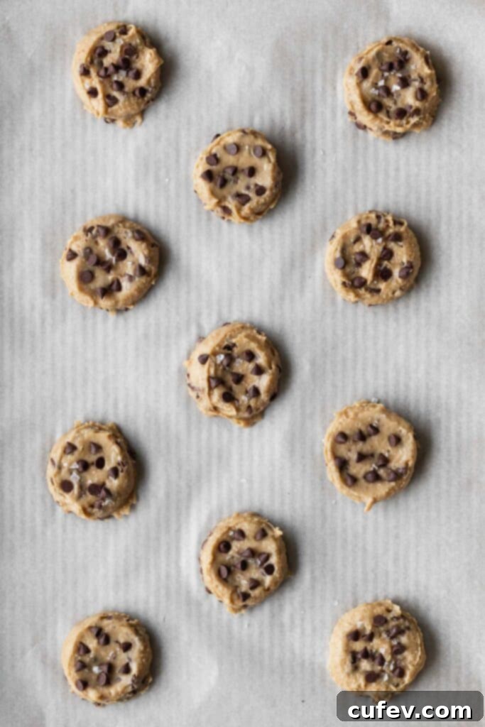Flattened chocolate chip cookie dough portions arranged on a baking sheet.