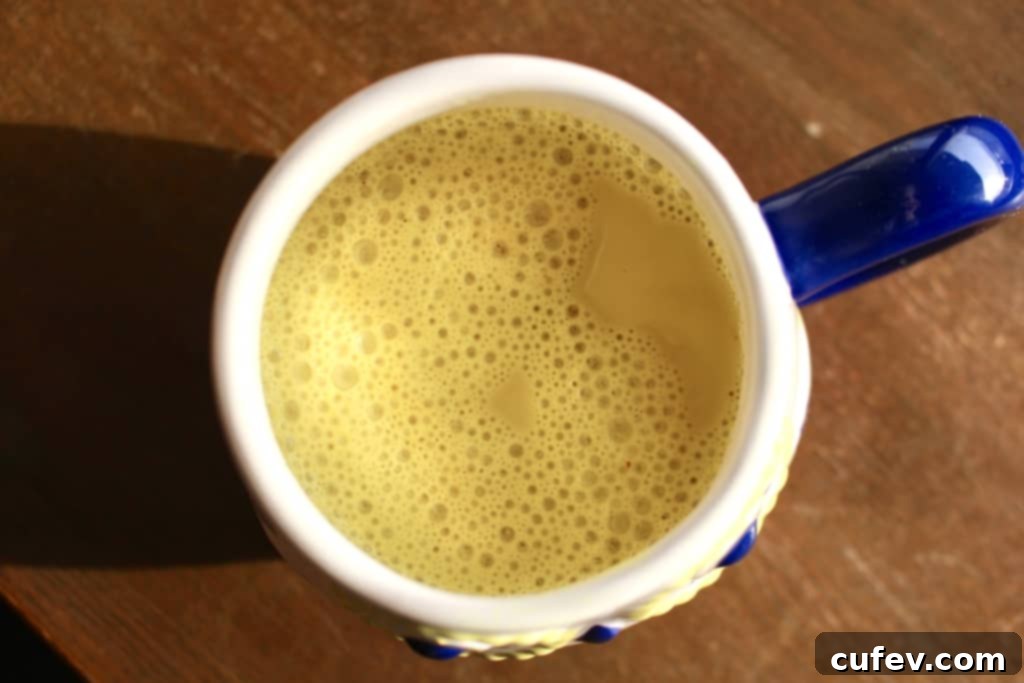 Freshly prepared golden milk in a mug, beside a jar of turmeric powder