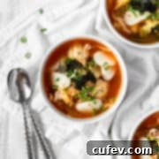 A bowl of Tteokguk (Korean rice cake soup) on a white surface with a couple silver spoons next to it, ready to be served.
