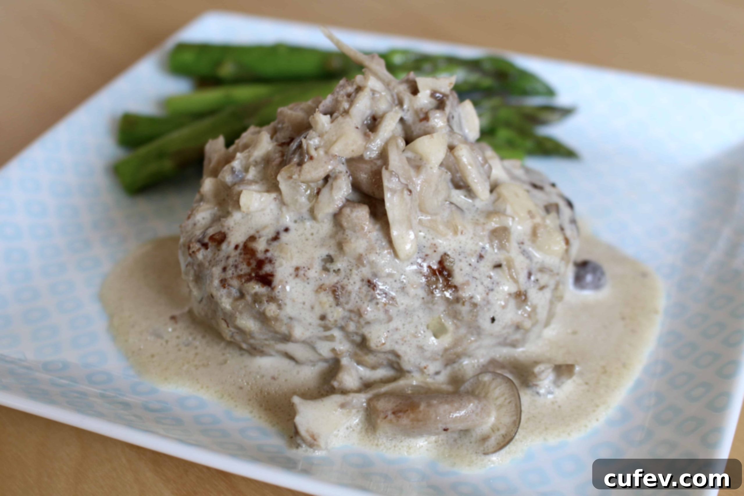Creamy mushroom sauce simmering around Salisbury steak patties in a frying pan
