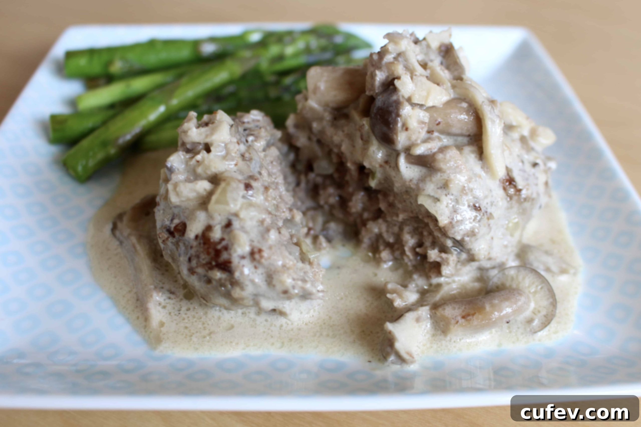 Salisbury steak with creamy mushroom sauce served alongside roasted asparagus and cherry tomatoes