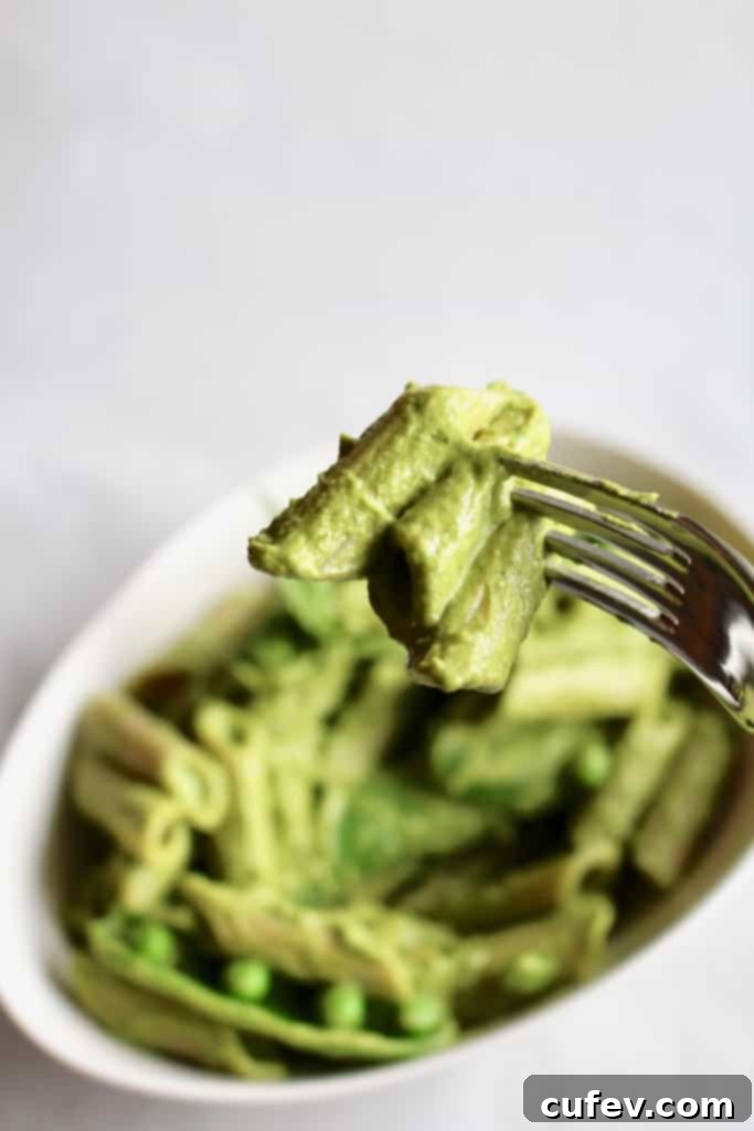 Close-up of a spoon scooping green vegan mac and cheese from a bowl, showing creamy texture.