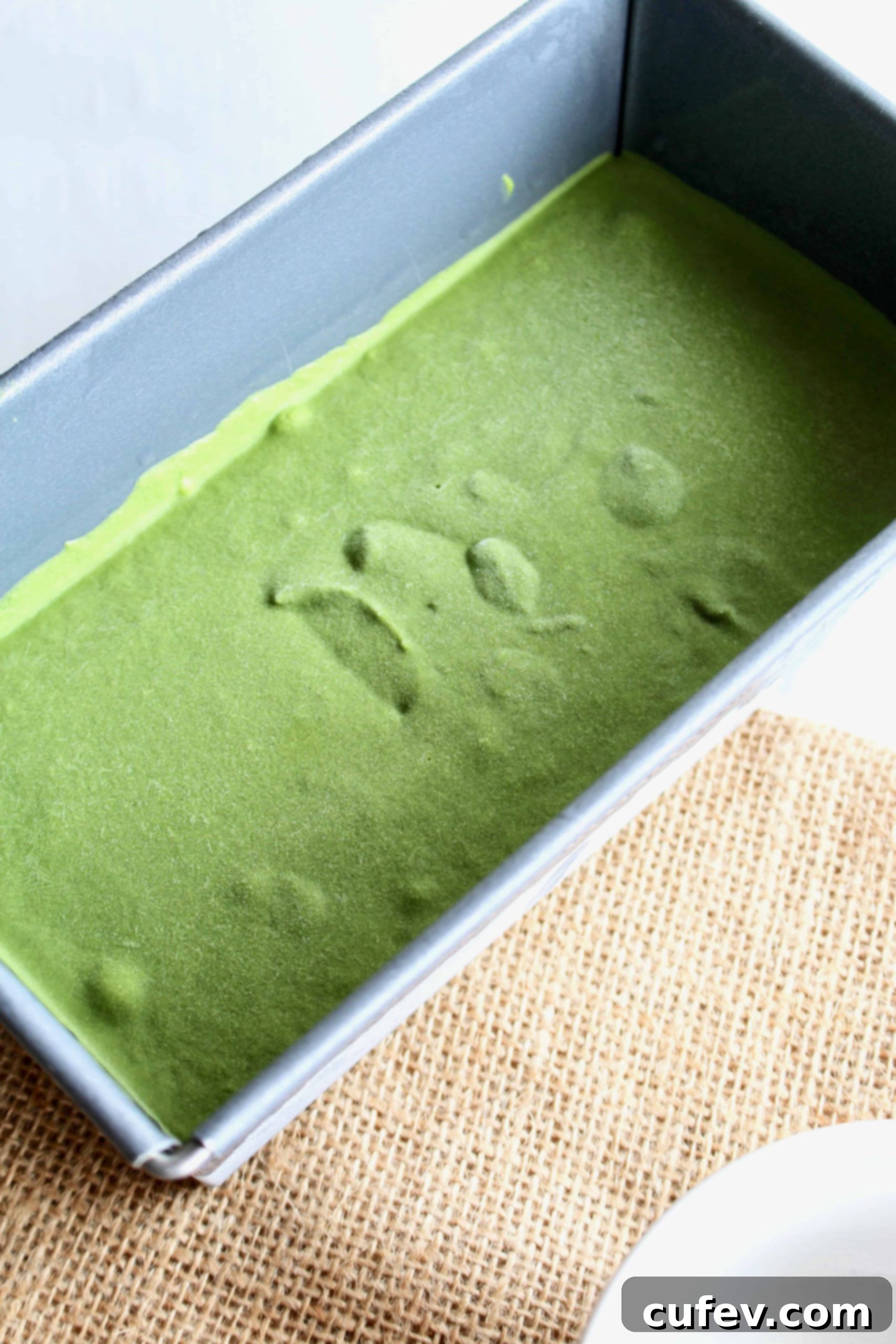 Vibrant green vegan matcha ice cream set in a white loaf pan, ready to be scooped and enjoyed.