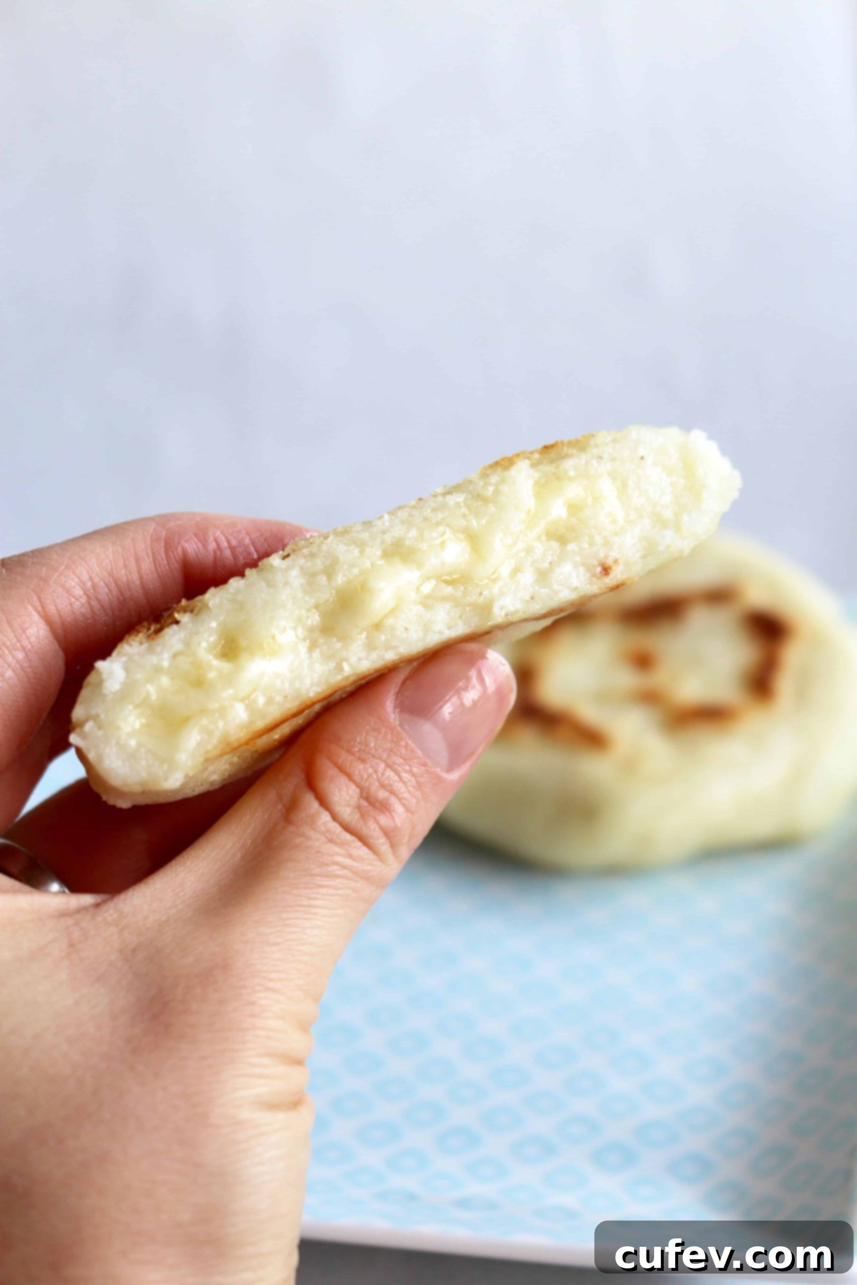 A hand holding a freshly cooked arepa, sliced open to reveal melty cheese bubbling inside. The golden-brown exterior contrasts with the soft, white interior.