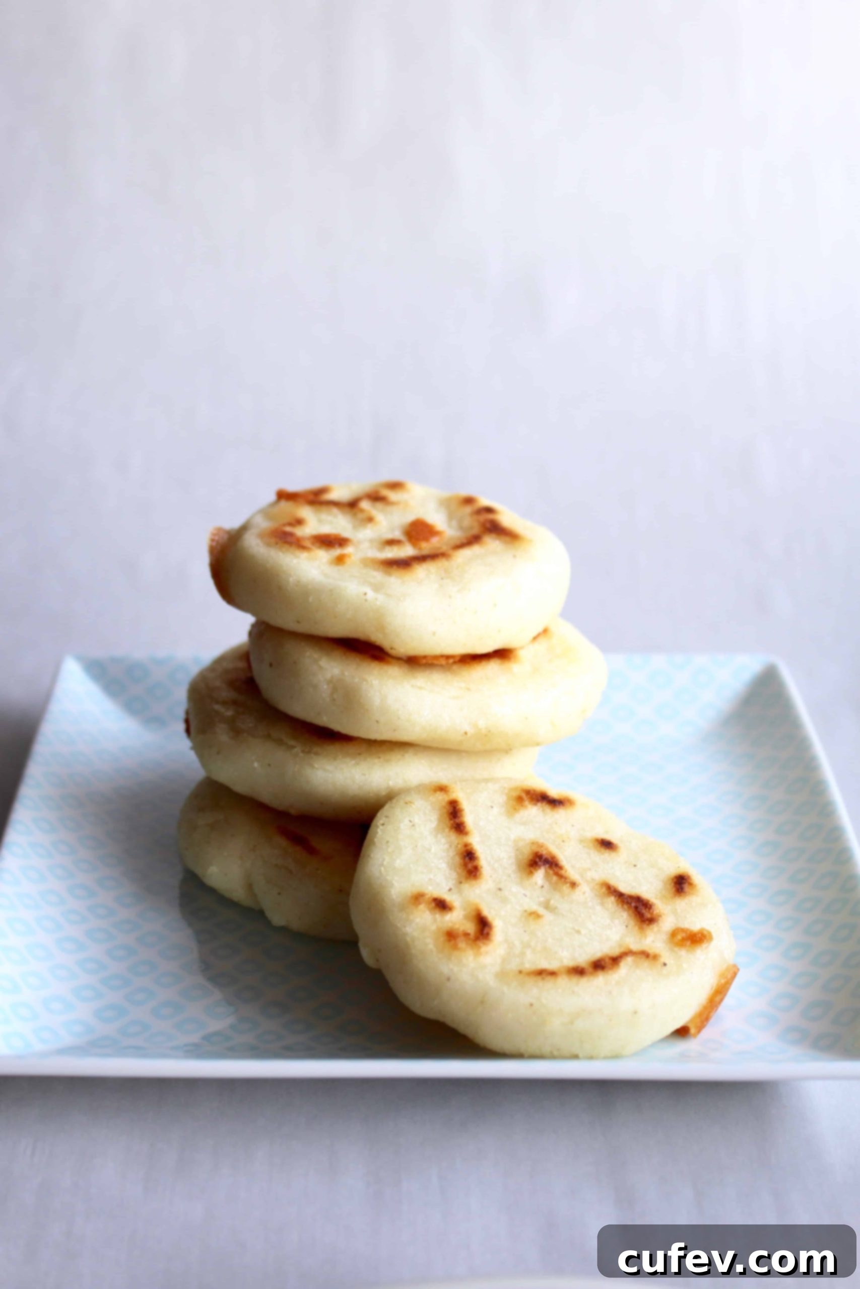 A perfectly stacked pile of freshly cooked arepas on a rustic square plate, ready to be served and filled. Their golden crust looks inviting.