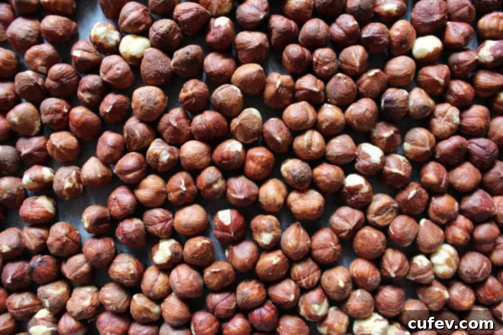 Close-up of raw hazelnuts spread in a single layer on a parchment-lined baking sheet, ready for roasting.