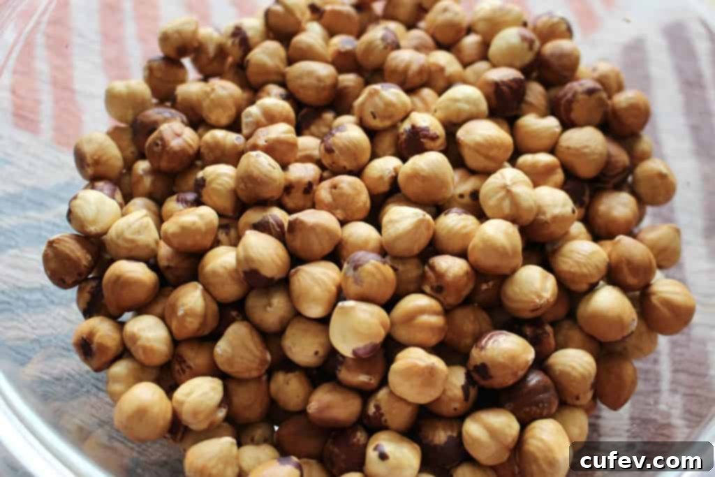 A bowl of roasted and peeled hazelnuts, with a few skins still clinging, showcasing their readiness.