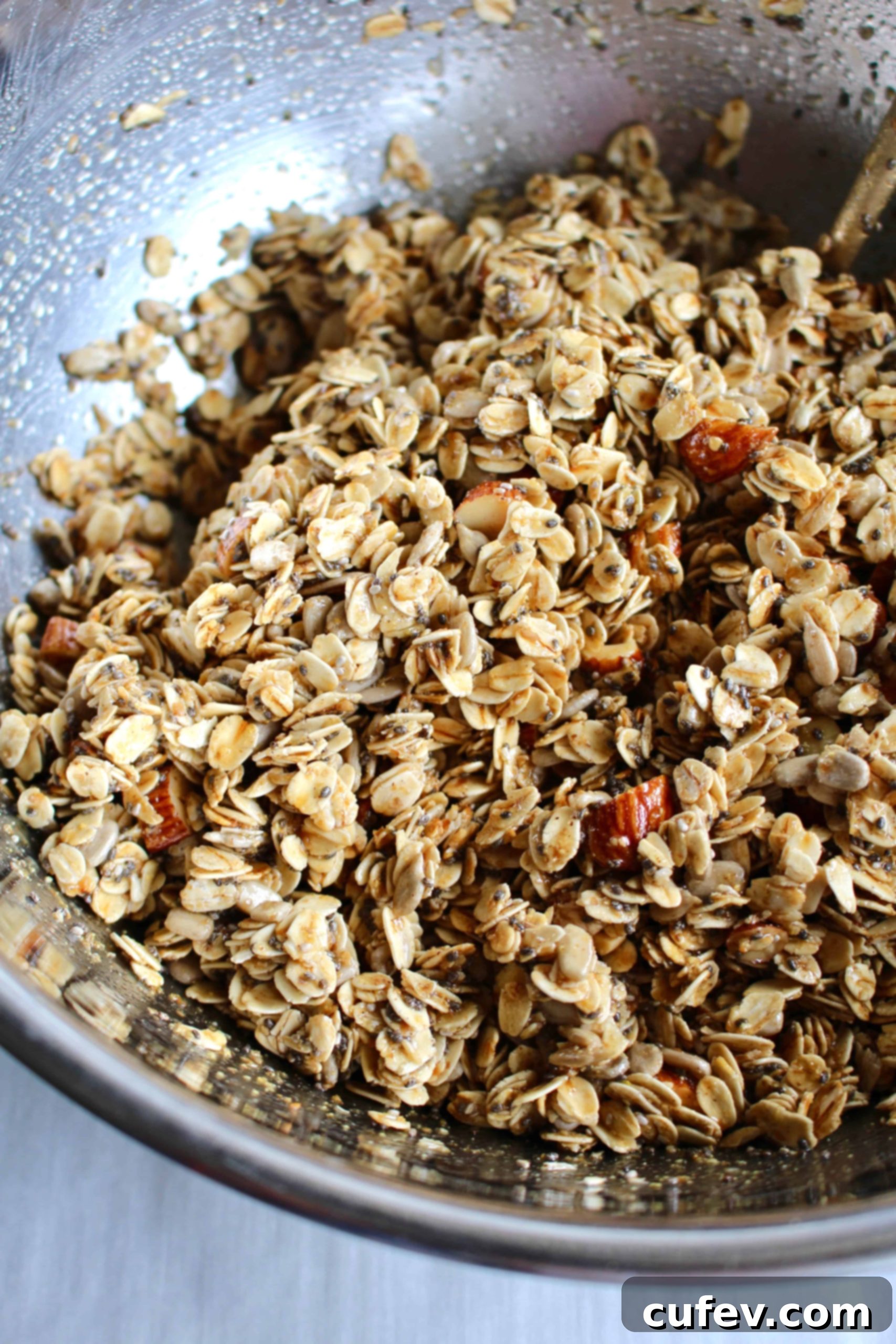 Gluten-free granola ingredients perfectly mixed in a large metal bowl, ready for baking.