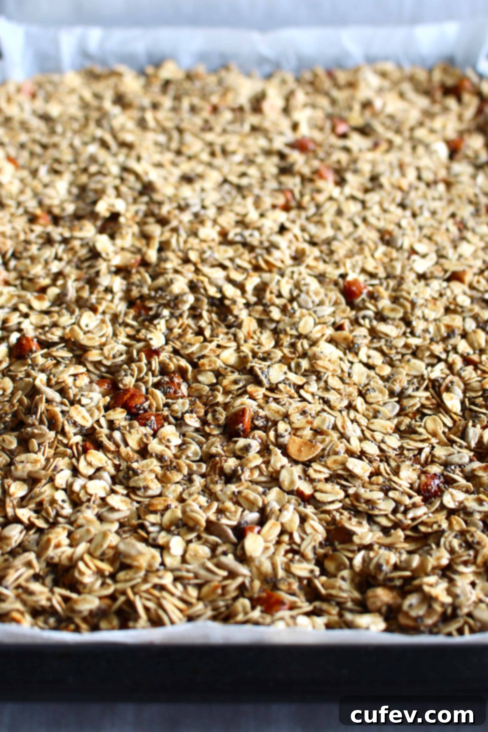 Gluten-free granola mixture spread evenly onto a parchment-lined baking sheet, prepared for the oven.