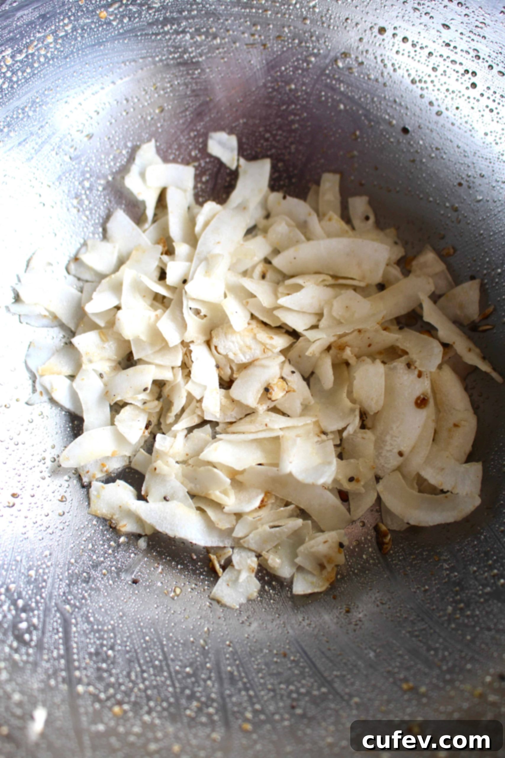 Unsweetened coconut flakes lightly tossed in a metallic bowl with a hint of maple syrup, ready to be added to the granola.