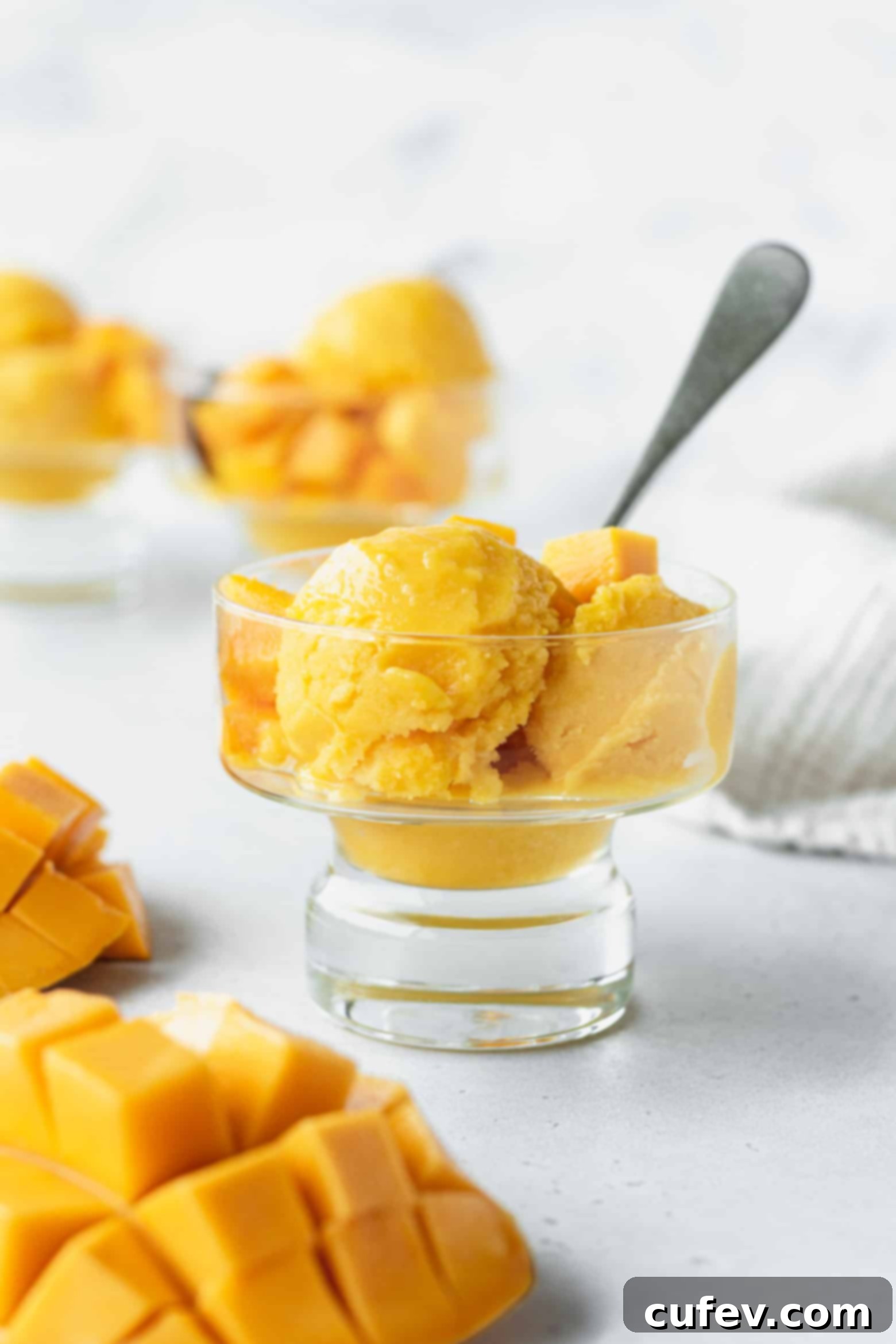 Two Ingredient Mango Sorbet 2 Scoops of vibrant mango lime sorbet in a elegant glass bowl, garnished with fresh mint