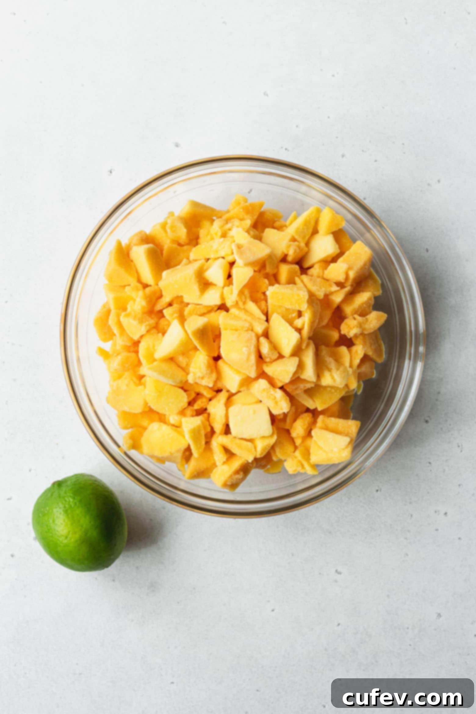 Two Ingredient Mango Sorbet 3 A bowl of frozen mango chunks next to a whole green lime, ready for blending